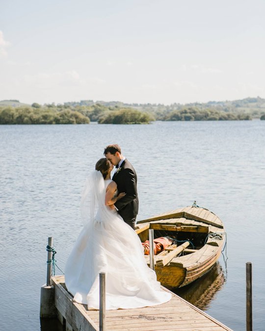 A couple kissing by a lake in wedding clothing 