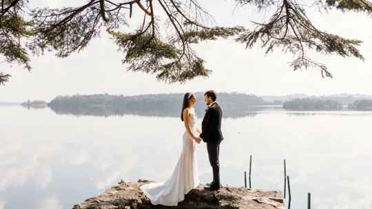 Wedding couple stood facing each other with a lake in the background